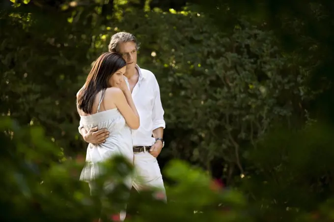 Husband and wife stand in embrace outdoors.