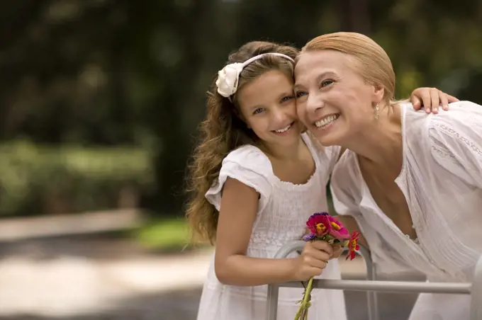 Grandmother and her granddaughter laugh together holding a bunch of flowers.