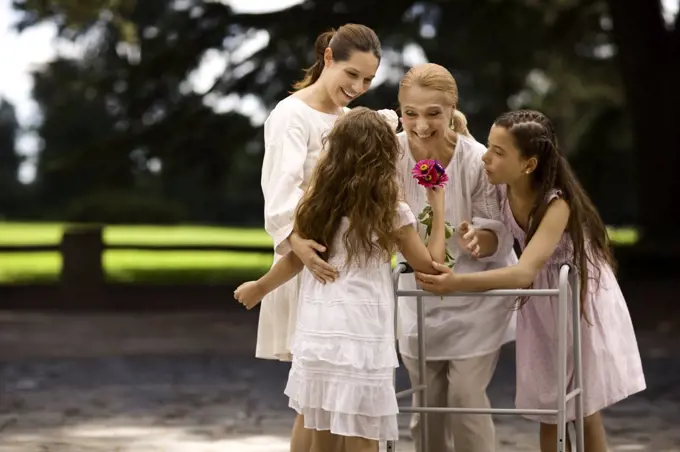 Grandmother and her daughter and granddaughters stand together outdoors as she is presented a bunch of flowers.