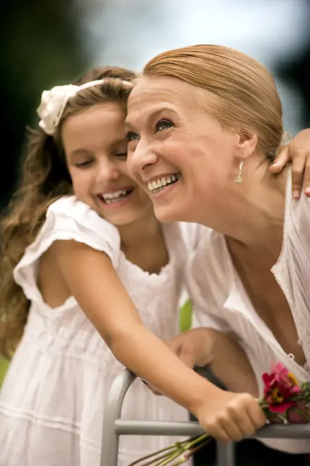 Grandmother and her granddaughter laugh together holding a bunch of flowers.