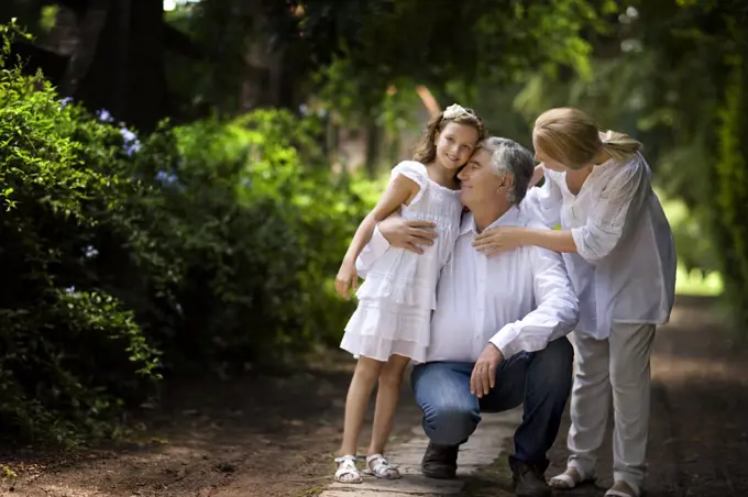 Grandparents stand with their granddaughter on a quiet country road.