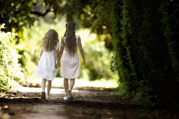 Two young girls hold hands and walk down a quiet country road.