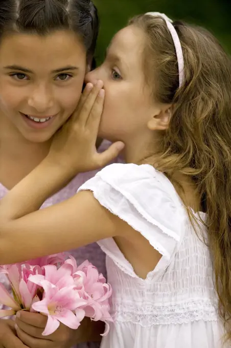 Young girl whispers in her sisters ear.