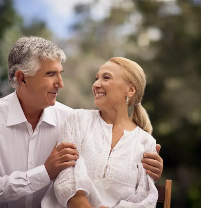 Elderly couple look into each others eyes while sitting outdoors.