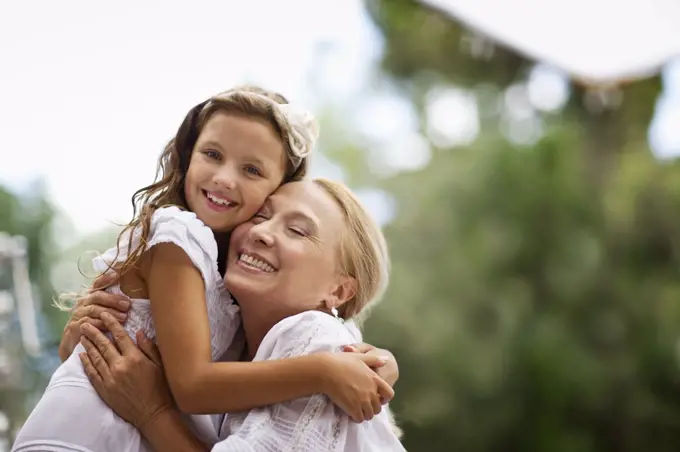 Grandmother embraces her granddaughter outdoors.