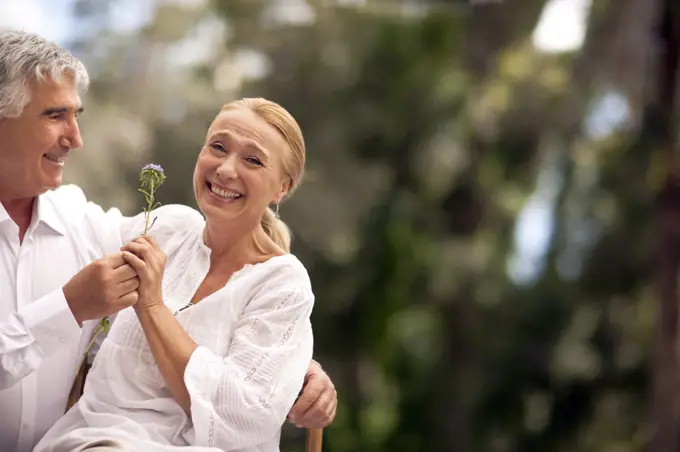 Husband gives his wife a flower as they sit outdoors.