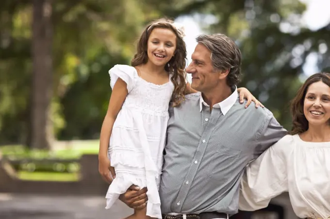 Father holds his daughter in his arms while standing beside his wife.