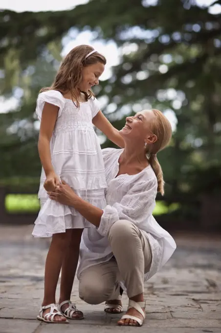 Grandmother crouches beside her young granddaughter and holds her hand outdoors.