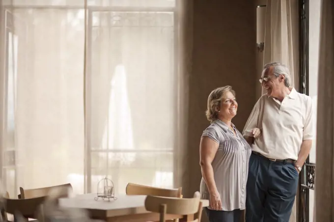 Happy mature couple standing in dining room. 