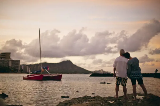 Couple watching sunset from waterside rocks. 