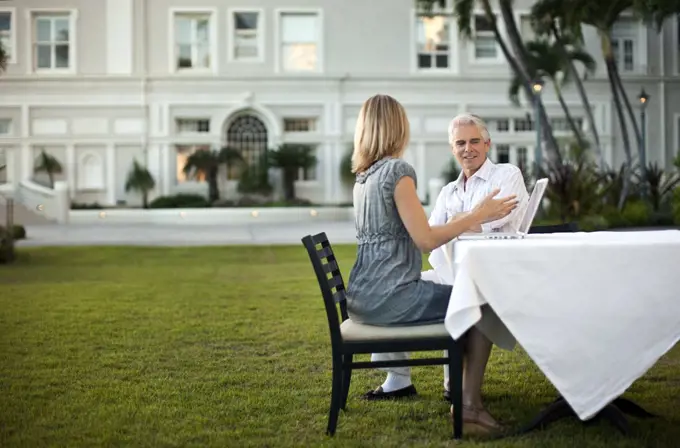 Husband and wife sitting in front of their hotel and using the laptop.