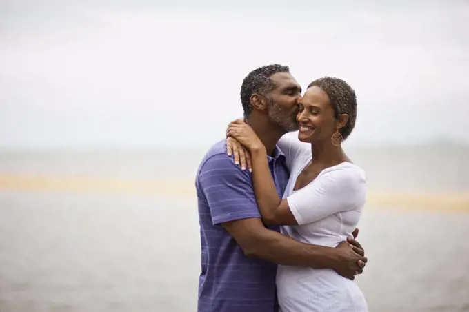 Mature man kissing his wife on the beach.