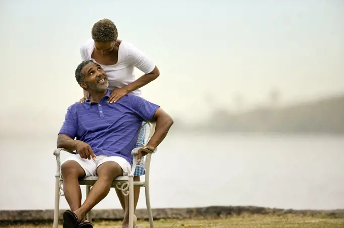 Mature man receiving shoulder massage from his wife by the beach.