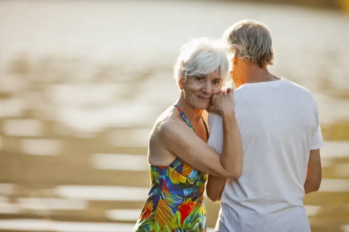 Portrait of a smiling senior woman leaning on the shoulder of her husband next to a lake.