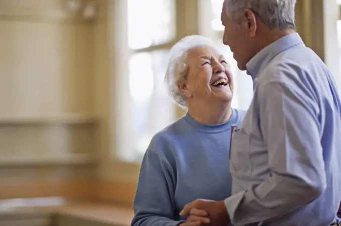 Happy senior couple dancing together in a room.