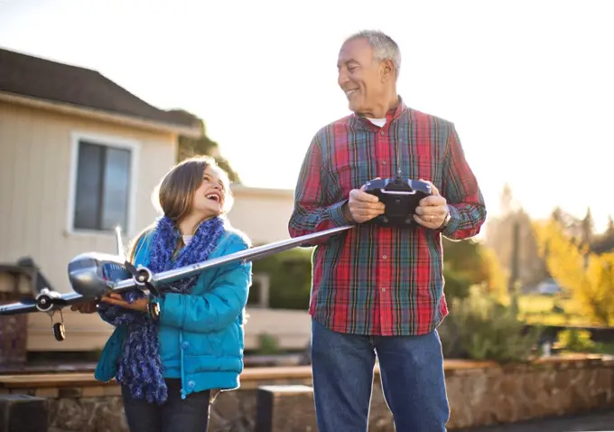 Smiling girl and her grandfather having fun playing with a toy airplane together in the back yard.