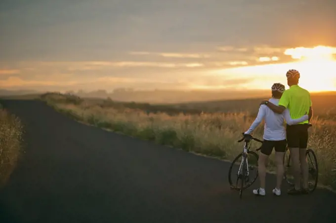 Mature couple embracing while watching the sunset over a rural landscape.