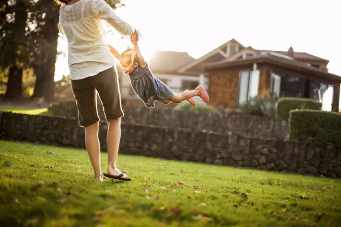 Young woman playfully spinning her happy young daughter around.