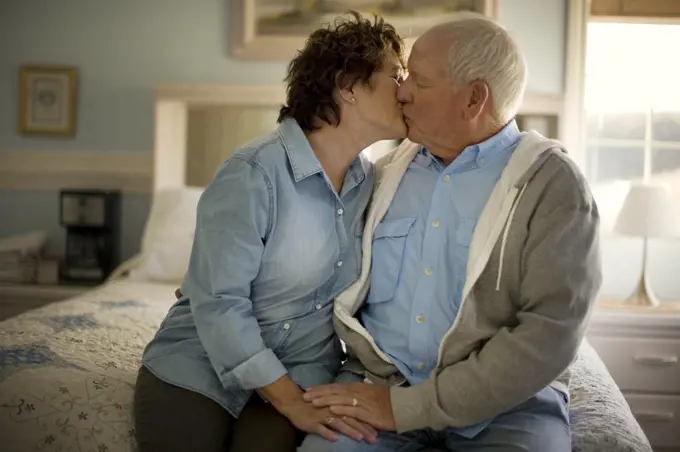 Affectionate mature couple share a passionate kiss while sitting on the bed.