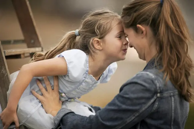 Smiling young mother holds her little girl who is sitting on a ladder.