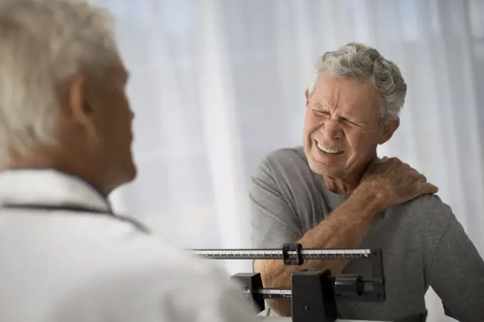 Mature man grips his shoulder in pain while attending a medical examination.