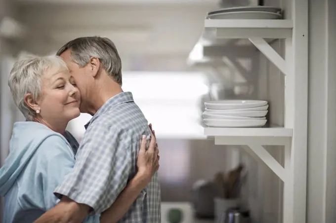 Affectionate mature couple tenderly embrace in the kitchen.