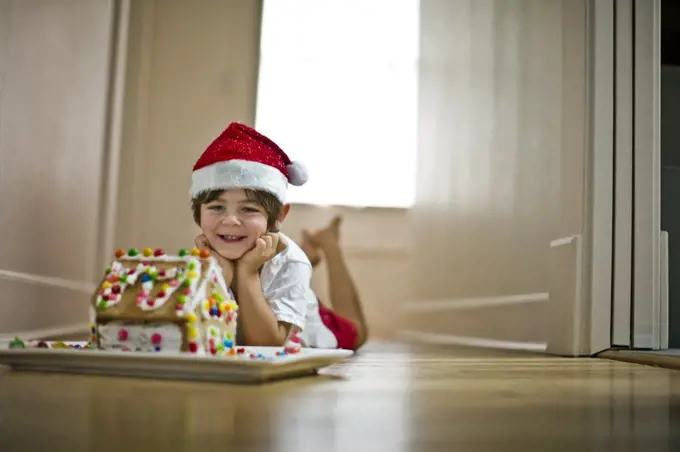 Young boy wearing a Santa hat next to a gingerbread house.