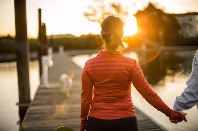 Couple walking hand in hand along a pier at sunset.