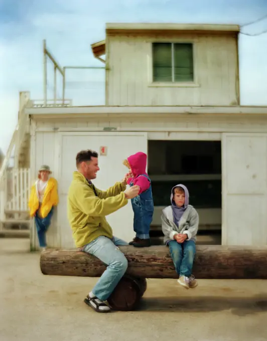 Side view of a father playing with his kids in front of a house.