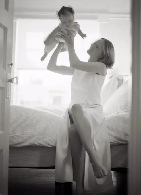 A mother is playing with her baby in the bedroom.