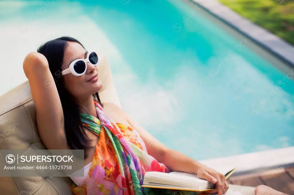 Serene woman relaxing, reading book at summer poolside