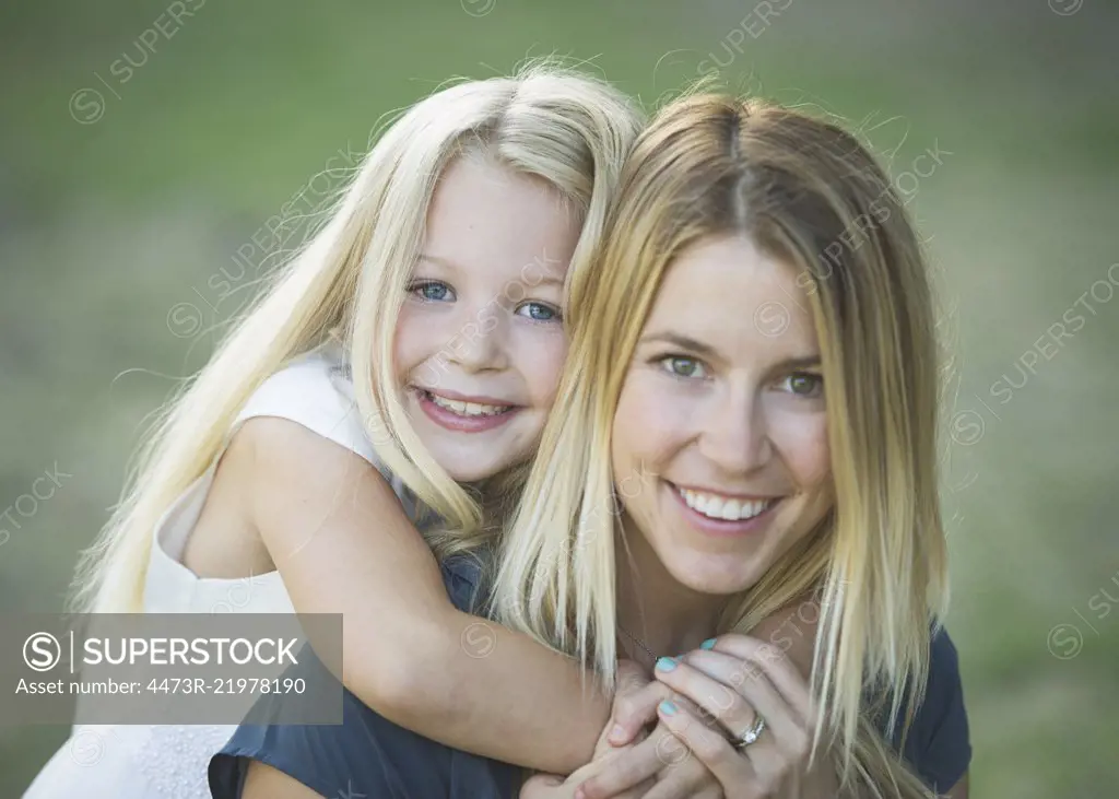 A woman and a young girl with her arms around the adult's neck hugging her and smiling at the camera.