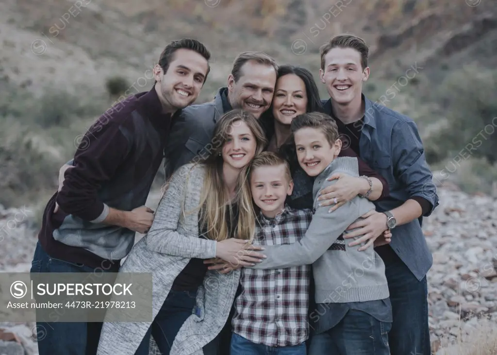 A large family group, four adults, men and women, three young people, two boys all hugging and posing for a photograph. 