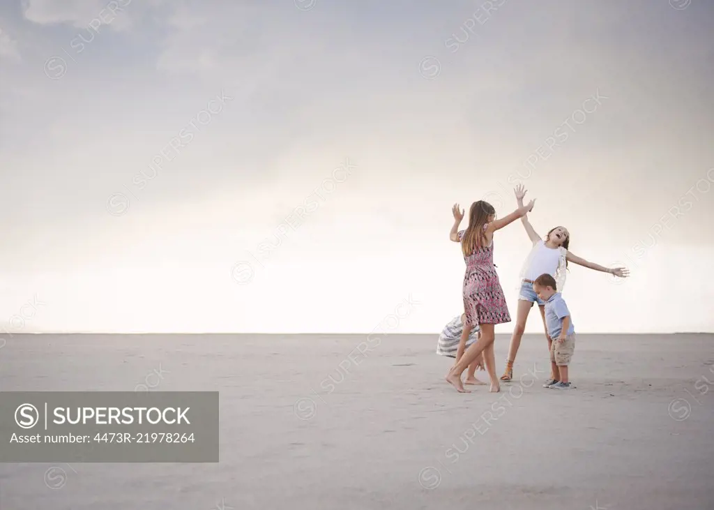 Four children on the beach, arm raised playing, three girls and one younger boy.