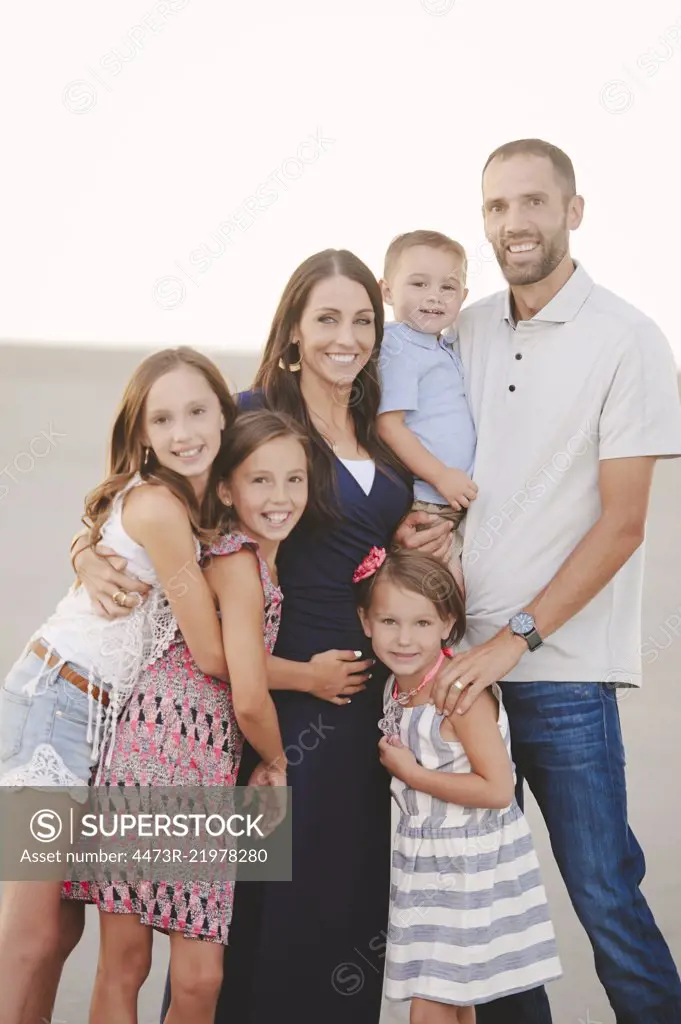 Two parents and four children, close together on the beach looking at the camera. 