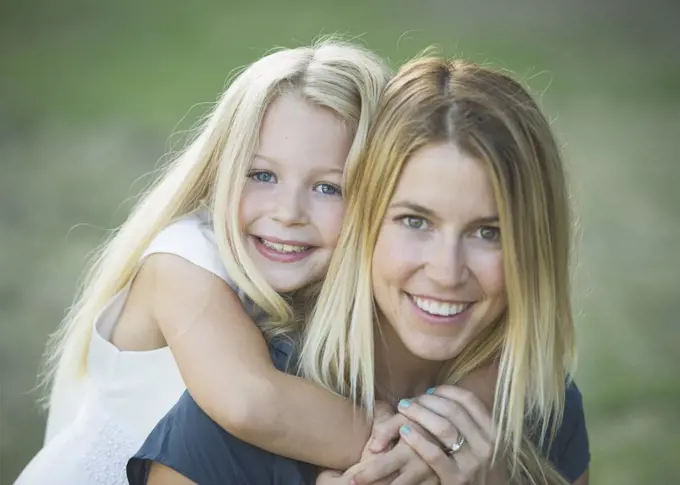 A woman and a young girl with her arms around the adult's neck hugging her and smiling at the camera.