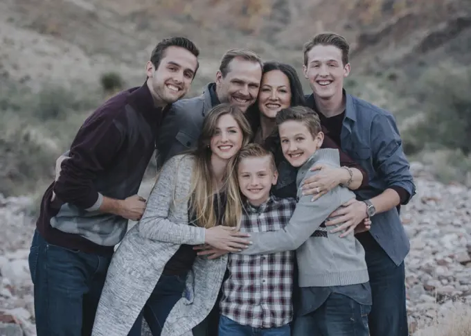 A large family group, four adults, men and women, three young people, two boys all hugging and posing for a photograph. 