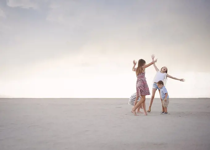 Four children on the beach, arm raised playing, three girls and one younger boy.