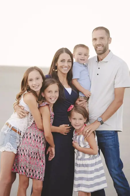 Two parents and four children, close together on the beach looking at the camera. 