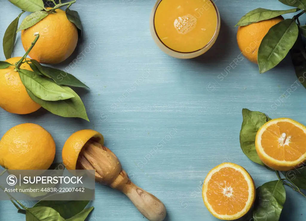 Fresh orange juice in glass and oranges with leaves on wooden turquoise blue painted background. Top view, copy space