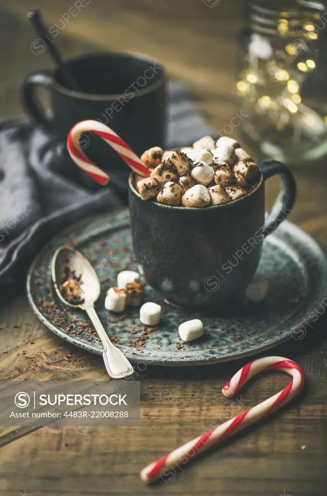 Winter warming sweet drink hot chocolate with marshmallows and cocoa in mug with Christmas holiday candy cane on wooden background, selective focus, copy space