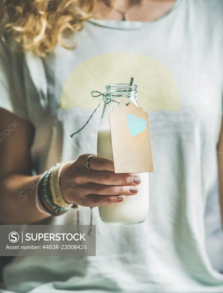 Young blond woman in grey light holding bottle of dairy-free almond milk in her hand. Clean eating, vegan, vegetarian, dieting, healthy food concept