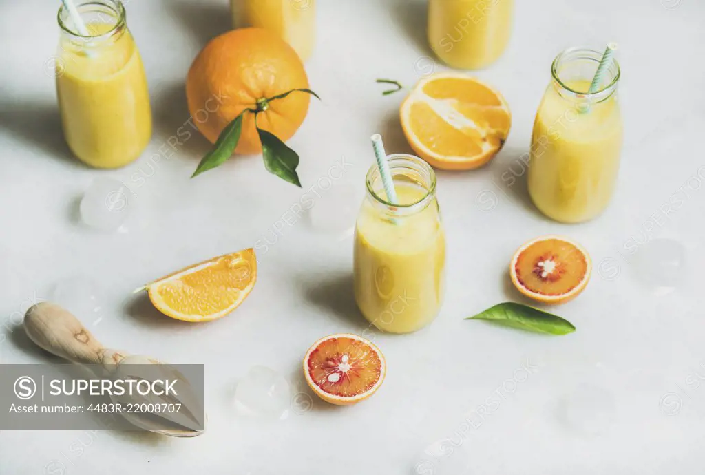 Healthy yellow smoothie with citrus fruit, ginger, ice in glass bottles over light marble table background, selective focus. Clean eating, vegan, vegetarian, detox, dieting food concept