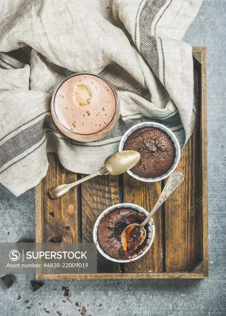 Chocolate souffle in blue individual baking cups and chocolate mocha coffee in wooden serving tray over grey concrete background, top view