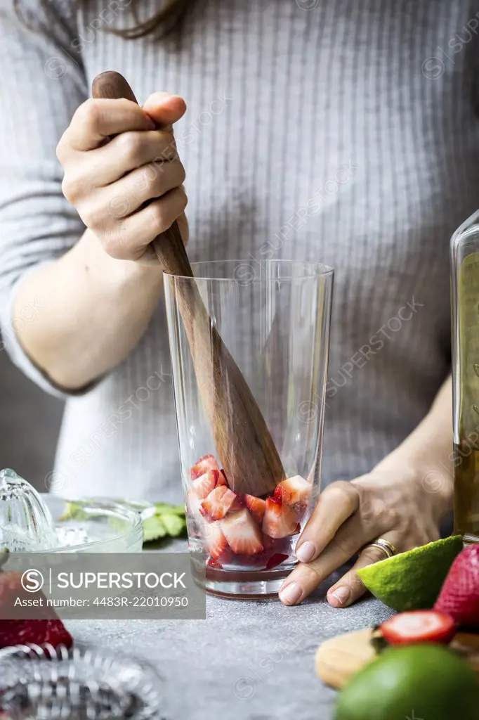 A woman is photographed as she is muddling strawberries to make margaritas.