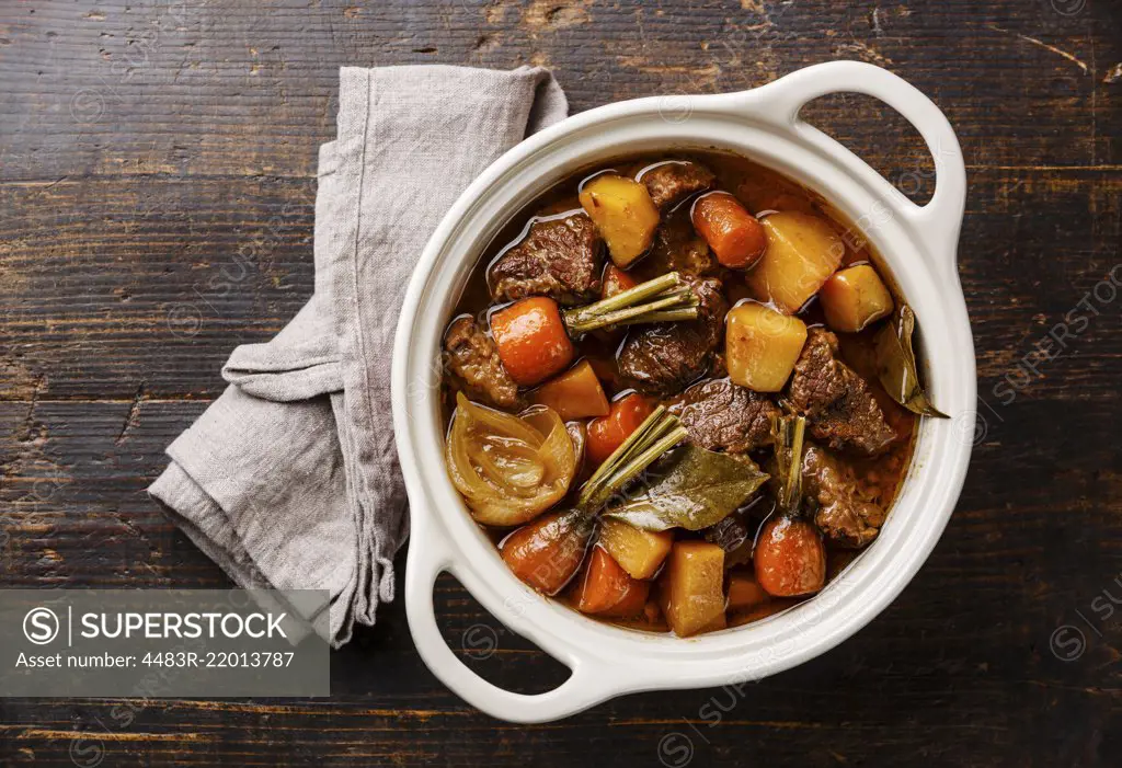 Beef meat stewed with potatoes, carrots and spices in ceramic pot on wooden background