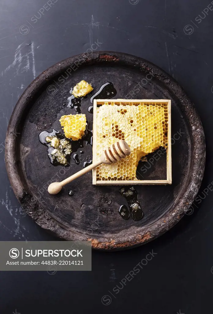 Honeycomb with wooden honey dipper on black textured background