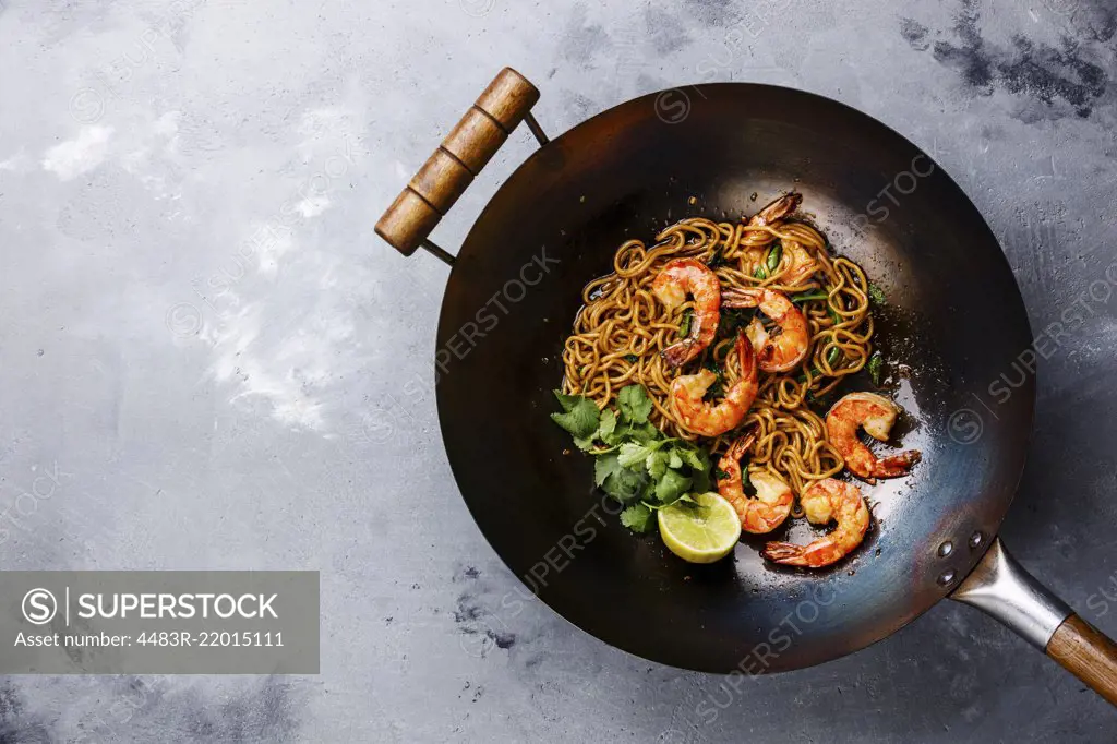 Ramen stir-fry noodles with shrimp in wok pan on gray concrete background copy space