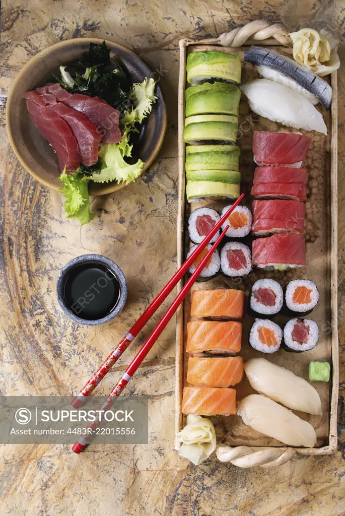 Sushi set nigiri, sashimi and rolls on clay plate served with chopsticks and soy sauce on stone surface. Flat lay.