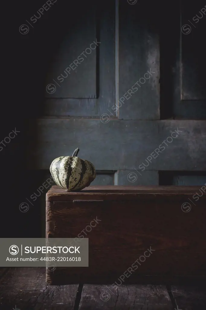 One decorative pumpkin on wooden chest over wooden background. Dark rustic style